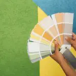 Hands holding a colorful paint swatch fan against a two-tone green and white background while learning how to choose interior paint colours.