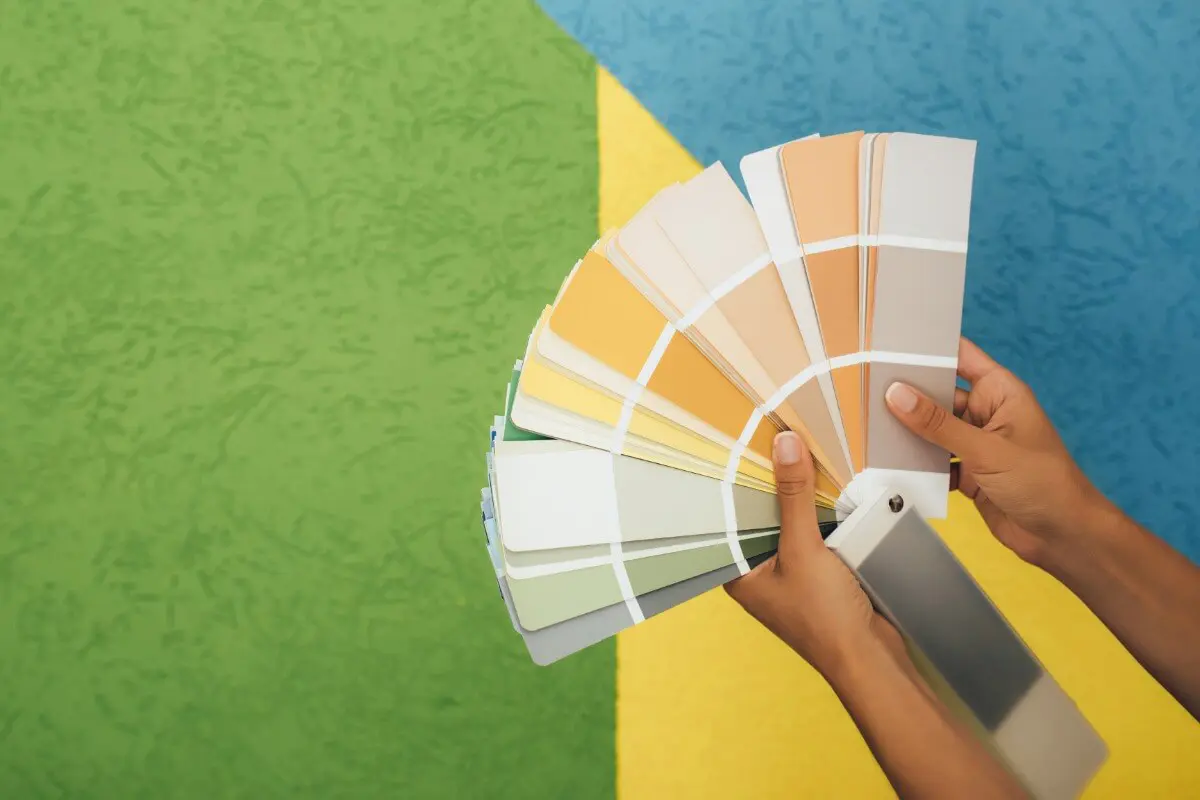 Hands holding a colorful paint swatch fan against a two-tone green and white background while learning how to choose interior paint colours.